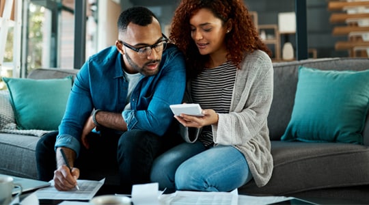 Man and woman look at papers and calculator to make a budget.